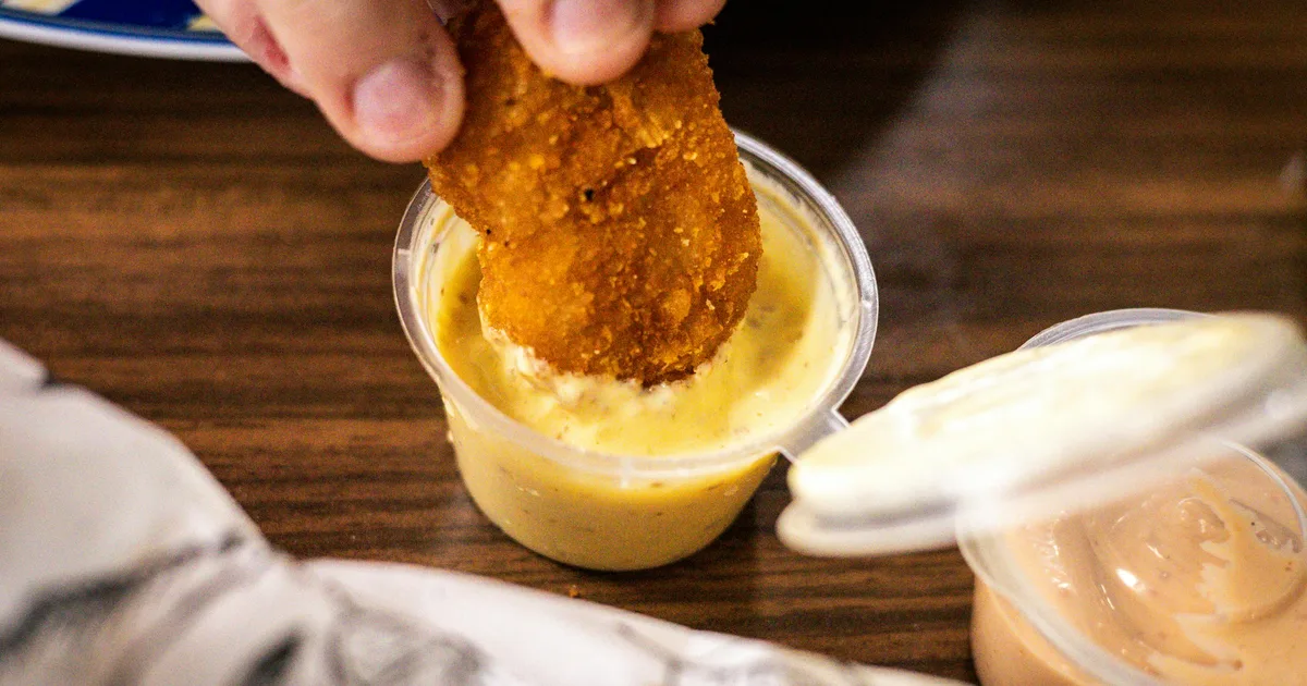 A crispy chicken bite being dipped into ranch sauce — the Dave's Hot Chicken Fallout Saucy Survival Kit