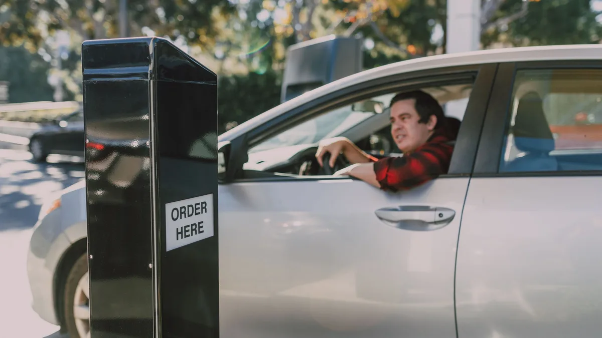 A driver ordering at a fast-food drive-thru kiosk — Dave's Hot Chicken drive-thru availability