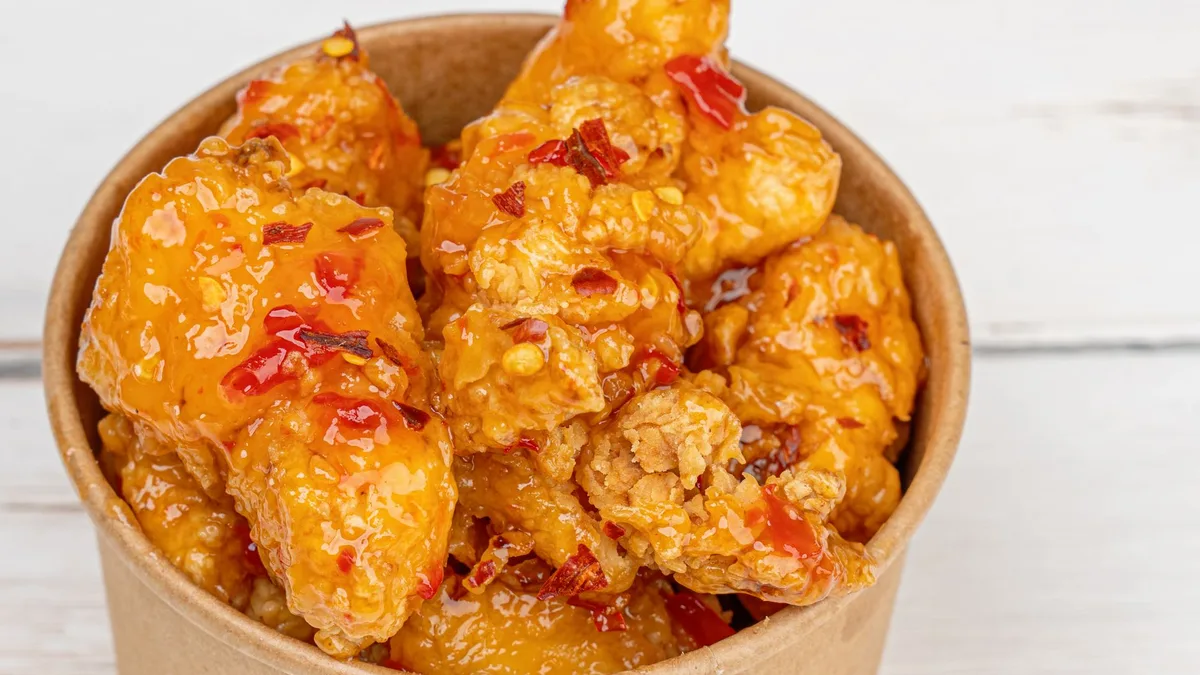 Crispy boneless fried chicken pieces in a takeaway box — Dave's Hot Chicken Saucy Bites sauces
