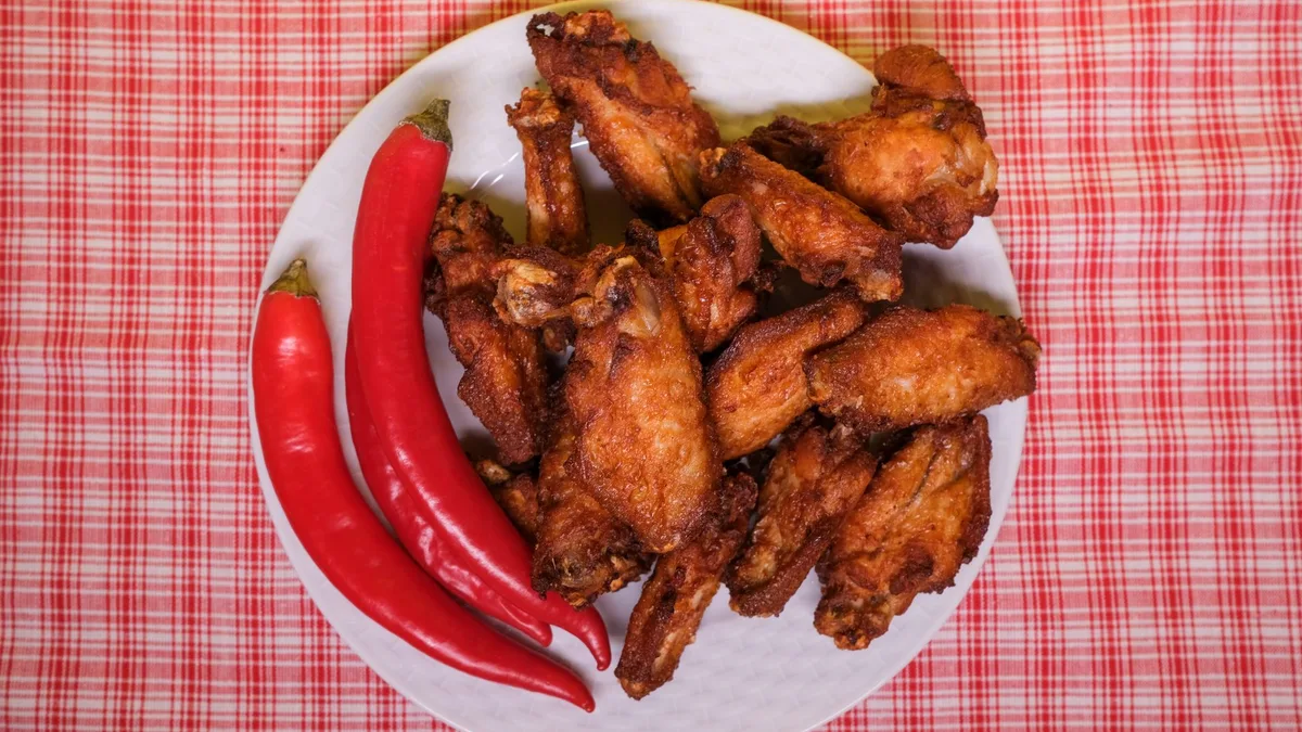 Spicy fried chicken on a plate with red chili peppers — Dave's Hot Chicken Reaper heat level