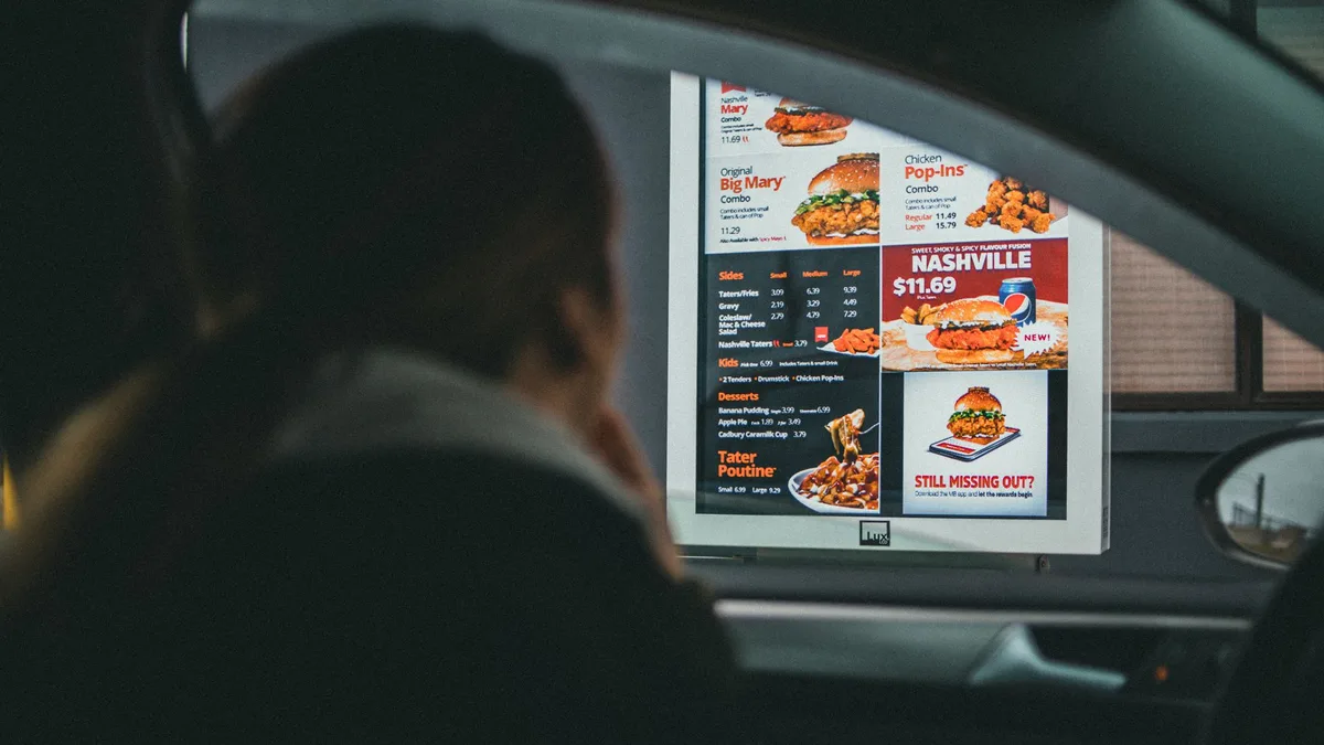 A person in a car viewing the menu at a fast-food drive-thru — Dave's Hot Chicken drive-thru hours
