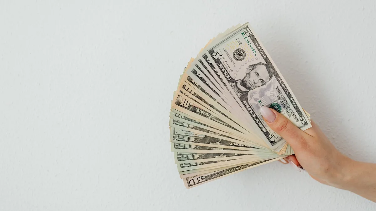 A hand holding fanned-out US dollar bills — the cost of a Dave's Hot Chicken meal